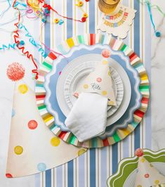 a table topped with plates and napkins on top of a striped table cloth covered in confetti