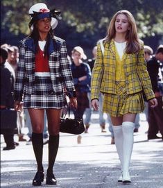 two women walking down the street in short skirts and plaid jackets, one wearing knee high socks