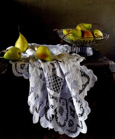 a glass bowl filled with pears on top of a table next to a white doily