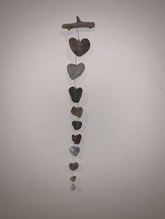 a metal heart mobile hanging on a wall next to a wooden stick with several hearts attached