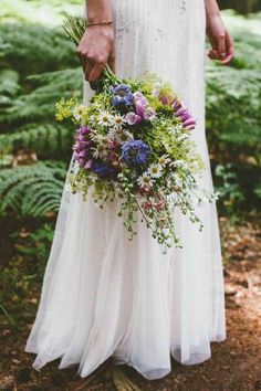 a woman in a white dress holding a bouquet of wildflowers and greenery