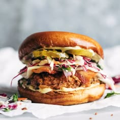 a chicken sandwich with coleslaw and pickles on it sitting on a napkin