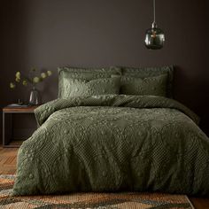 a bed with green bedspread and pillows in a dark room next to a table