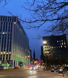 cars are driving down the street in front of some tall buildings at night with lights on