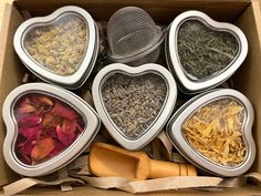 six heart shaped tins filled with different types of herbs and spices in them, sitting inside a cardboard box