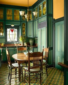 a kitchen with green cabinets and yellow floor tiles on the walls, an oval dining table surrounded by four wooden chairs