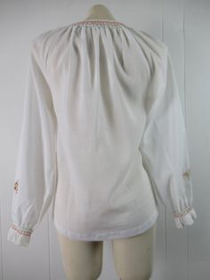 "Vintage 1970s peasant shirt ethnic blouse. Made of white poly/cotton. Has bohemian embroidery on front and arms. Tie at the neck. Made by Lily. About a size small/medium. Actual measurements are: 36\" at the bust 38\" at the waist 16\" shoulder to shoulder 22\" shoulder to end of sleeve 24.5\" overall length In very good condition." Traditional White Peasant Top For Fall, White Peasant Top With Boho Collar, White Boho Collar Peasant Top, Long Sleeve Peasant Top For Festivals, Folk Style Peasant Top With Boho Collar, Peasant Style Cotton Blouse For Fall, White Peasant Blouse For Fall, White Peasant Blouse For Fall Season, Peasant Style Long Sleeve Embroidered Top