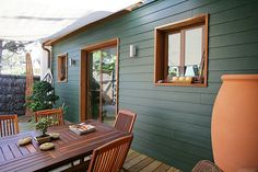 a wooden table sitting on top of a wooden floor next to a green house with windows