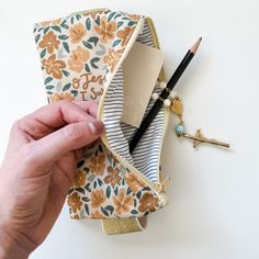 a person holding a pencil case in front of a white wall with flowers on it