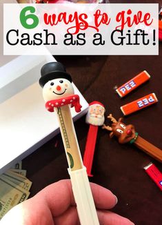 a person holding a pencil in their hand with money and candy on the table behind it