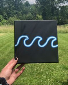 a hand holding up a black box with blue waves on it in front of trees