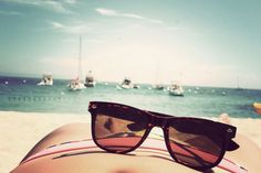 a person laying on top of a sandy beach next to the ocean with boats in the background