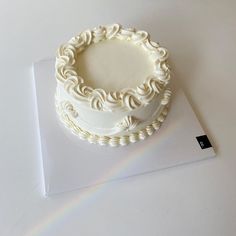 a white frosted cake sitting on top of a table next to a piece of paper