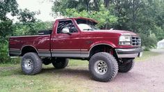 a red pick up truck parked on top of a dirt road next to some trees