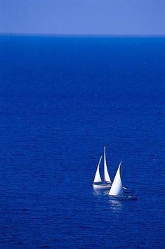 two sailboats in the ocean on a clear day