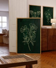 two framed flowers on a green wall in a room with wooden floors and white walls