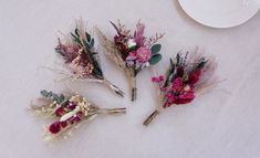 four dried flowers are arranged on a white tablecloth with a plate in the background