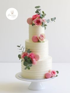 a three tiered cake with pink flowers and greenery on the top is sitting on a white pedestal