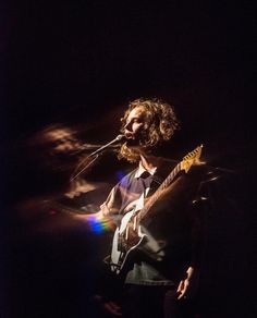 a man that is standing up with a guitar in front of him and singing into a microphone