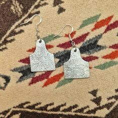 The classic, silver fashion of these earrings make them the perfect staple piece in your jewelry collection. Made of aluminum, they are very lightweight and easily worn. Due to the handcrafted nature of this item, the finished product may vary slightly from the photo. Stamped Metal Earrings For Gifts, Etched Metal Drop Earrings, Silver Etched Metal Earrings, Etched Silver Metal Earrings, Etched Metal Dangle Earrings, Cattle Tags, Country And Western, Engraved Earrings, Ear Tag