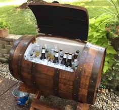 a wooden barrel filled with bottles of beer sitting on top of a stone floor next to a garden