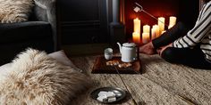 a woman sitting on the floor in front of a fire place with tea and marshmallows