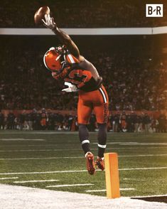 a football player jumping up into the air with a ball in his hand and an orange helmet on