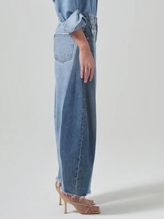 a woman standing in front of a white background wearing a blue shirt and jean pants