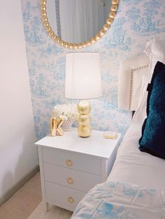 a bedroom with blue and white wallpaper, gold accents and a round mirror on the wall