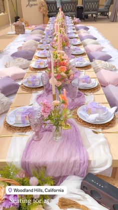 a long table is set up with purple and pink flowers, plates and napkins