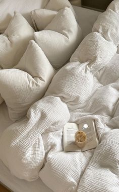 an unmade bed with white pillows and a book on the bottom shelf next to it