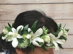 a woman wearing a flower crown with white flowers on her head and greenery in her hair