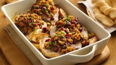 a casserole dish with meat and vegetables in it on a cutting board next to breadsticks