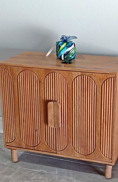 a wooden cabinet sitting on top of a cement floor next to a white wall with a blue and green object on it