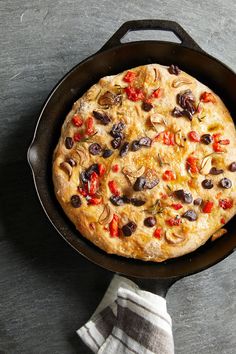 a pizza with olives, peppers and mushrooms in a cast iron skillet on a table