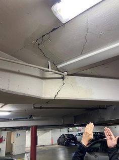 a man is holding his hand up to the ceiling in an empty parking garage with cars