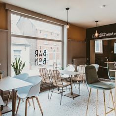 the interior of a restaurant with tables and chairs in front of large windows that look out onto an urban street