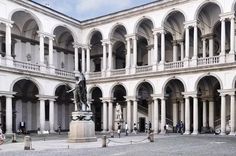 the courtyard of an old building with columns and arches on it's sides, as well as a statue in the center