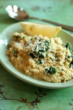 a white plate topped with mashed potatoes and spinach next to a lemon wedge