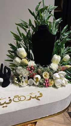 an arrangement of flowers and plants on a table with arabic writing in the middle,