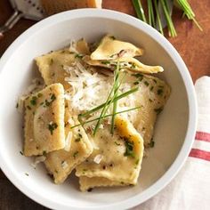 a white bowl filled with ravioli on top of a wooden table next to bread