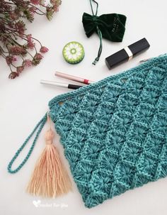 a crochet bag with some other items on it and a flower in the background