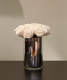 a vase with white roses in it on a black table next to a wall and a lamp