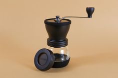 an espresso coffee maker with a black lid on a brown background, next to a grinder