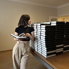 a woman standing in front of stacks of black and white books on a wooden table