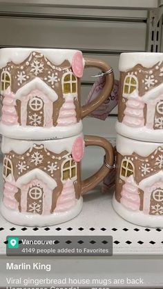 three coffee mugs decorated with gingerbread houses and snowflakes are on display