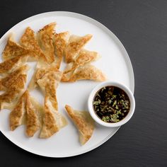 a white plate topped with dumplings next to a bowl of dipping sauce