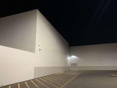 an empty parking lot in front of a white building with yellow lines on the ground