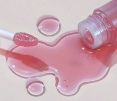 pink liquid spilling out of a bottle on top of a white surface with drops of water