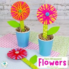 two flower potted plants sitting on top of a table with paper flowers in them